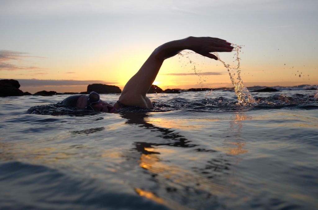 person swimming in body of water at sunset